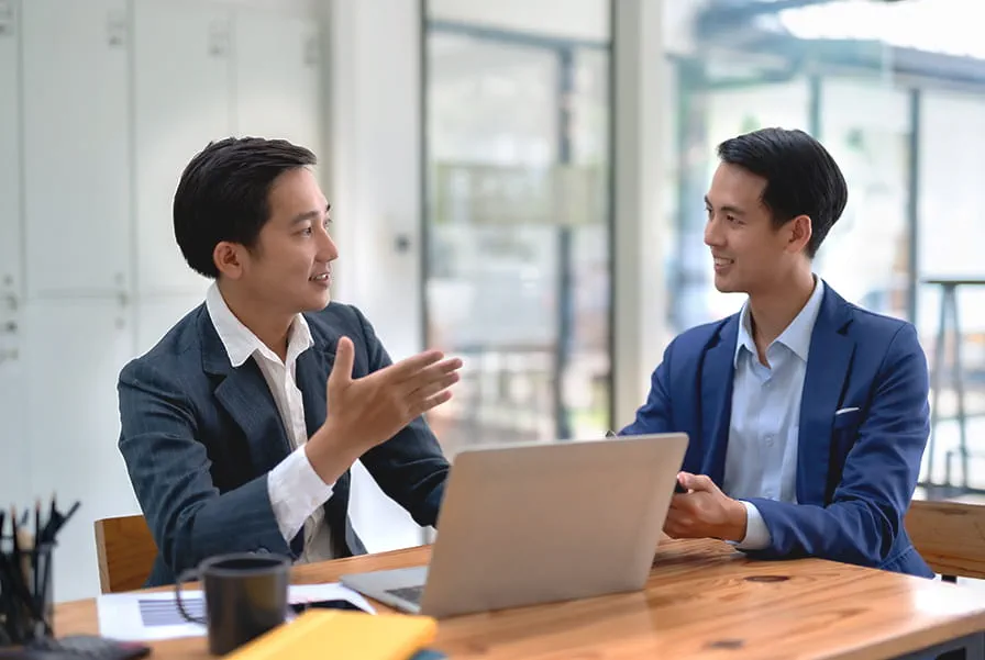 Two men in business suits having a discussion at an office desk.