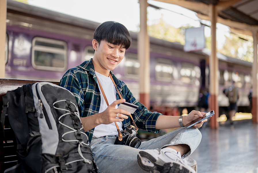 Young traveller managing expenses abroad using an RHB Multi Currency Account/-i to access foreign currencies while waiting at a train station.