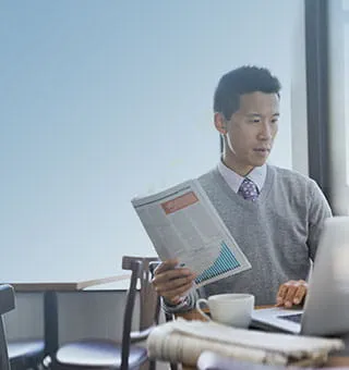 Asian guy using laptop while holding economic newspaper